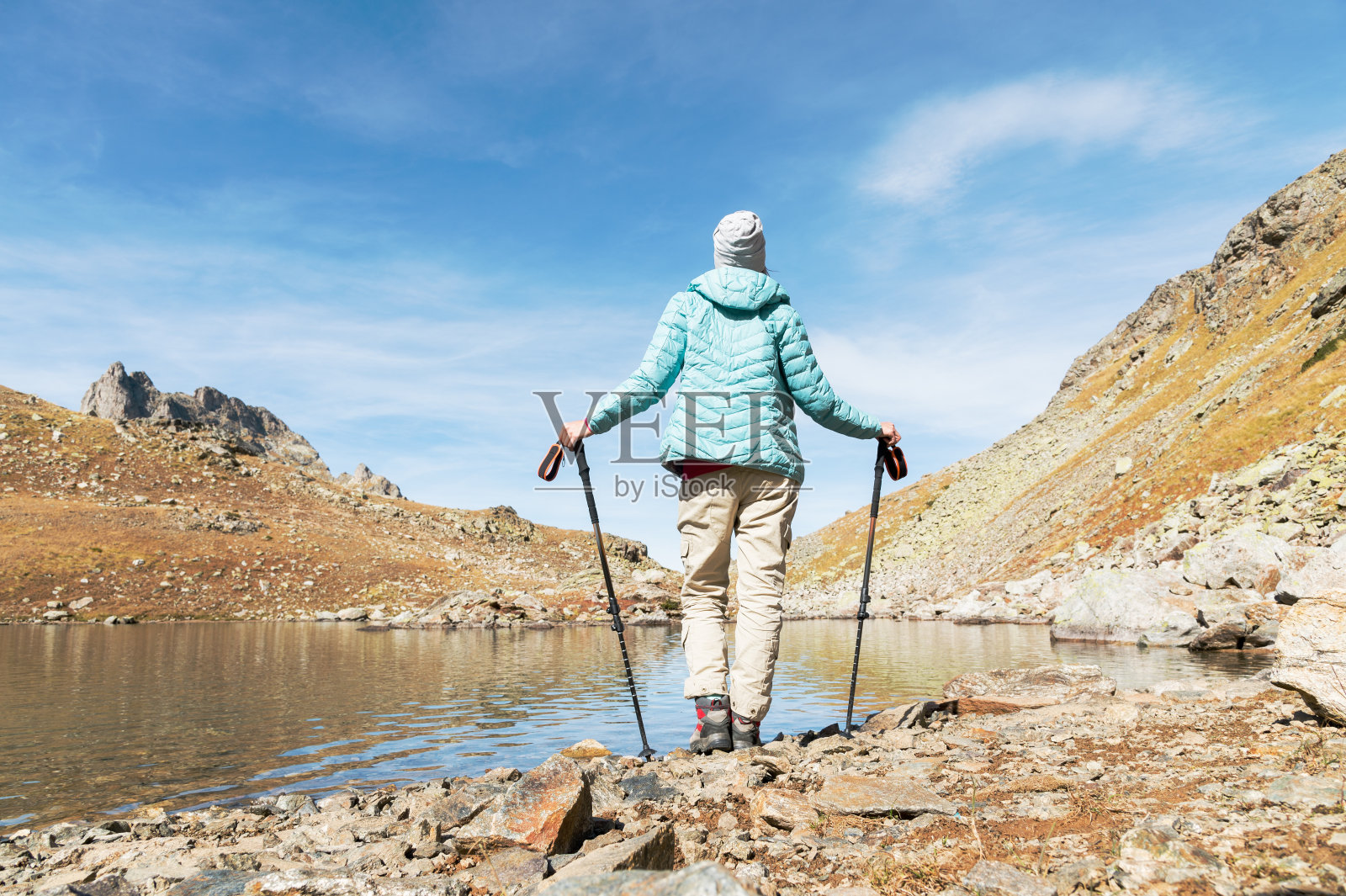一个瘦削的背包女孩拿着追踪棒站在高加索山脉的高山湖泊旁边照片摄影图片