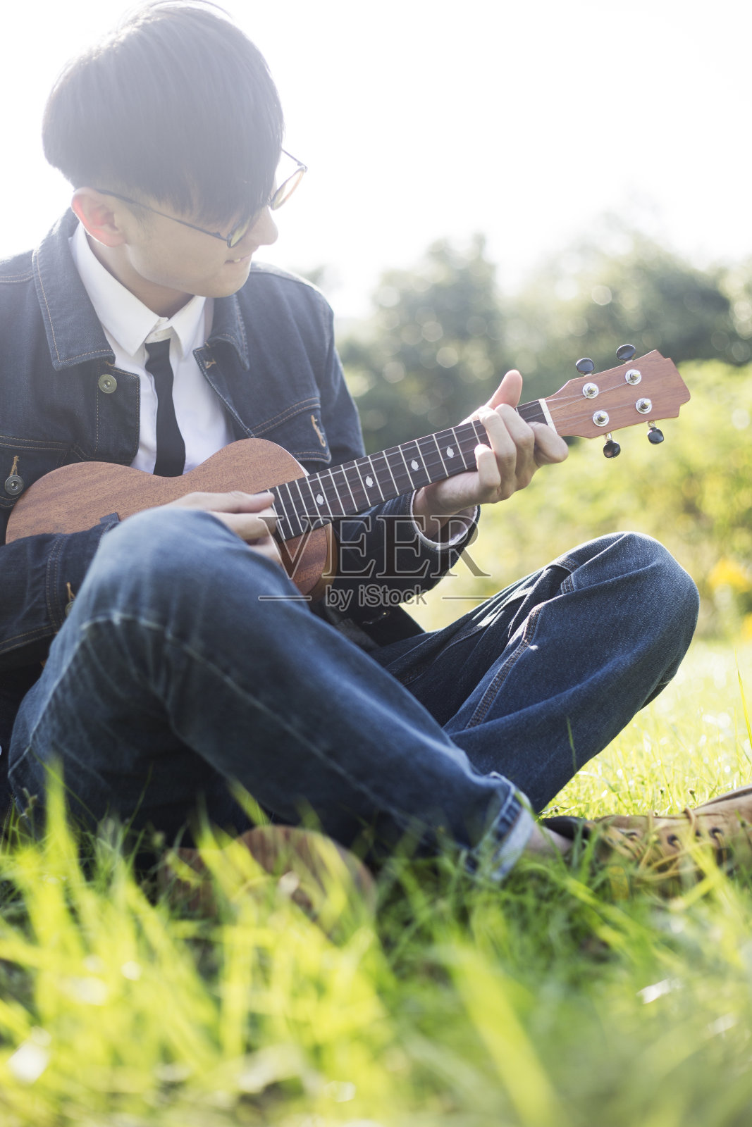 年轻人坐在草坪上弹着小吉他照片摄影图片