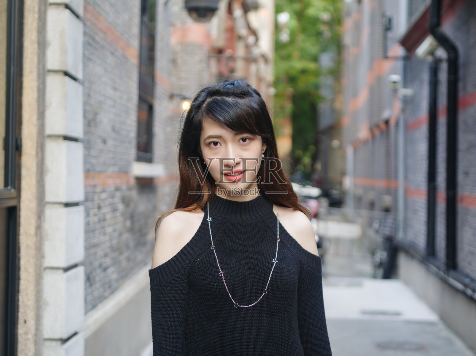 美丽的年轻中国女人的肖像穿着黑色管裙在上海新天地,她微笑在灰色的砖背景,快乐的时间,亚洲女孩的概念,旅游的概念。照片摄影图片