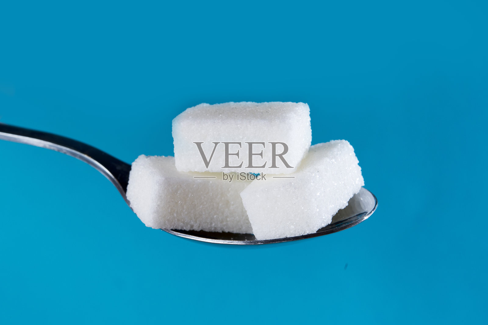近距离的茶匙与一堆糖块孤立的蓝色背景在糖和卡路里滥用和糖尿病和不健康的营养概念照片摄影图片