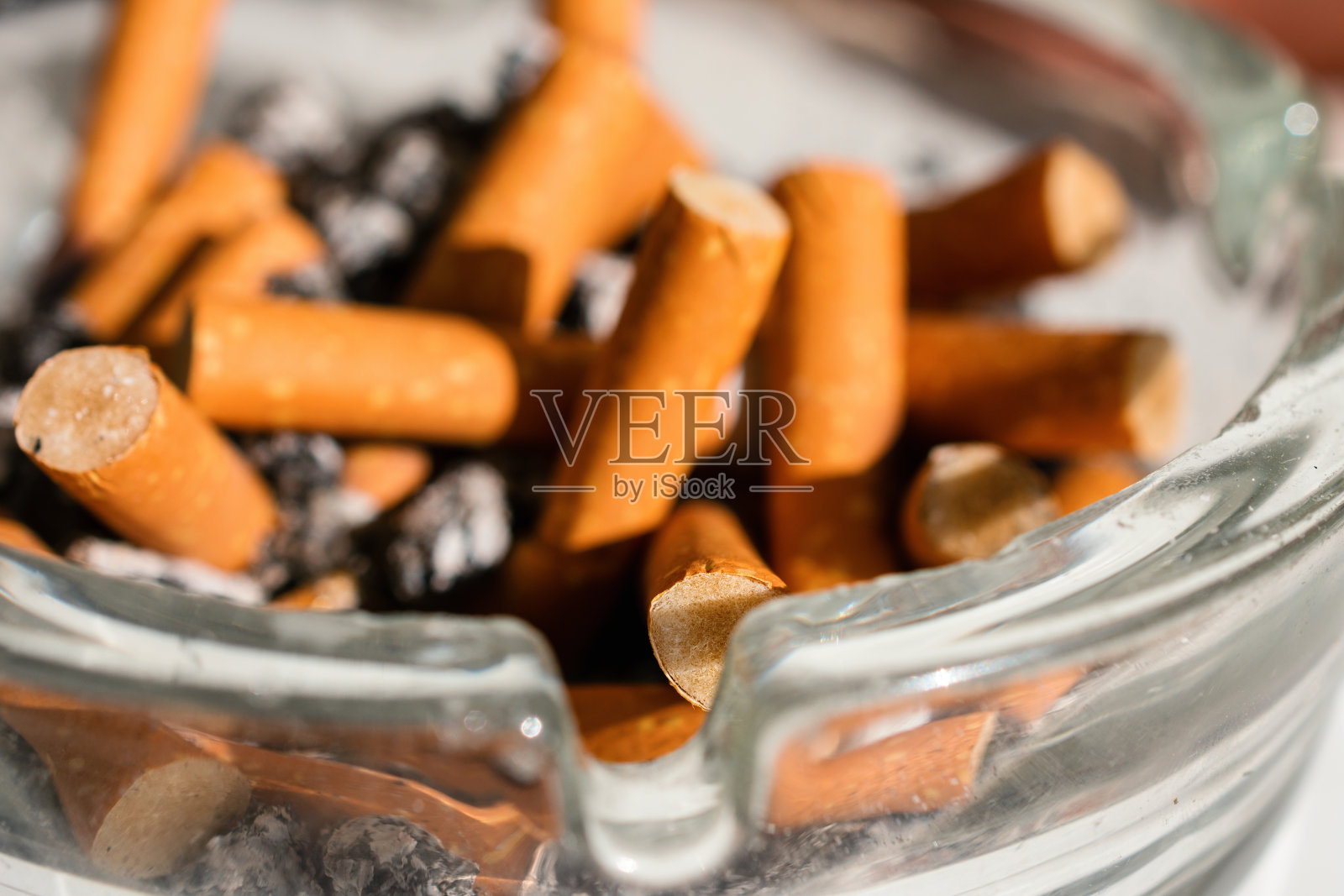 玻璃烟灰缸中装有橙色滤嘴的烟头照片摄影图片