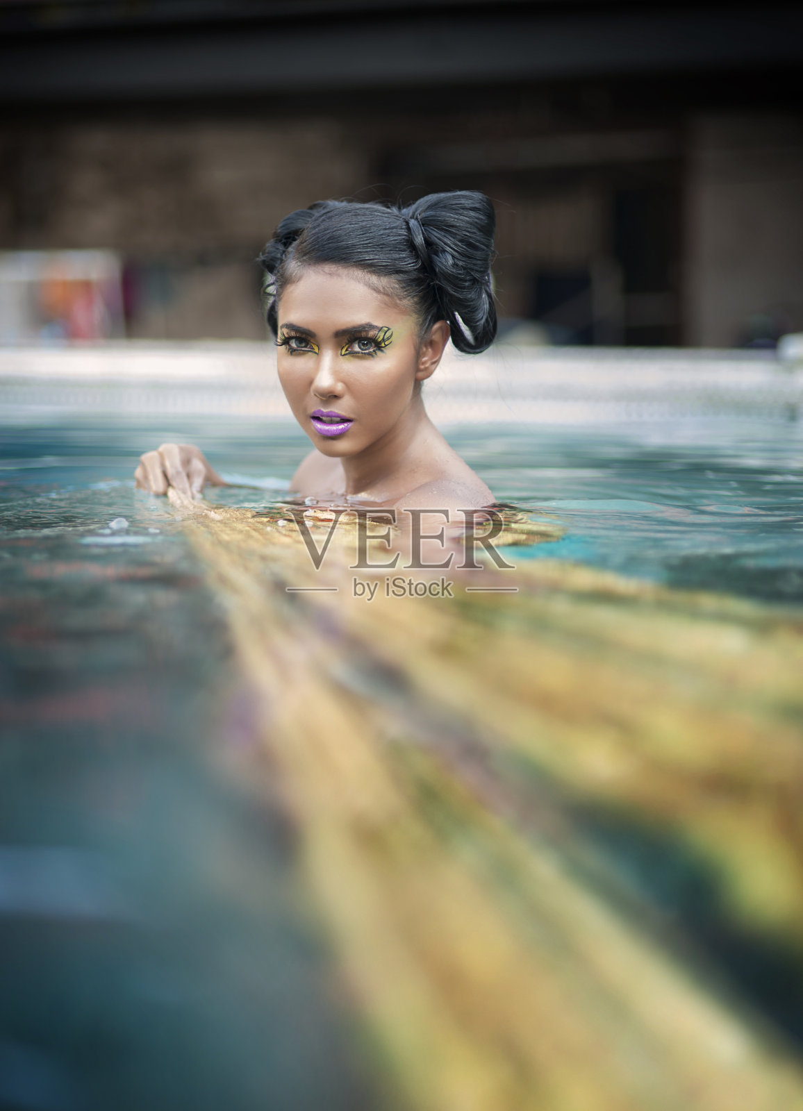 年轻的亚洲女人晒黑的皮肤和黑色光泽的头发在蓝色的金色比基尼游泳在游泳池,花哨的脸化妆。照片摄影图片