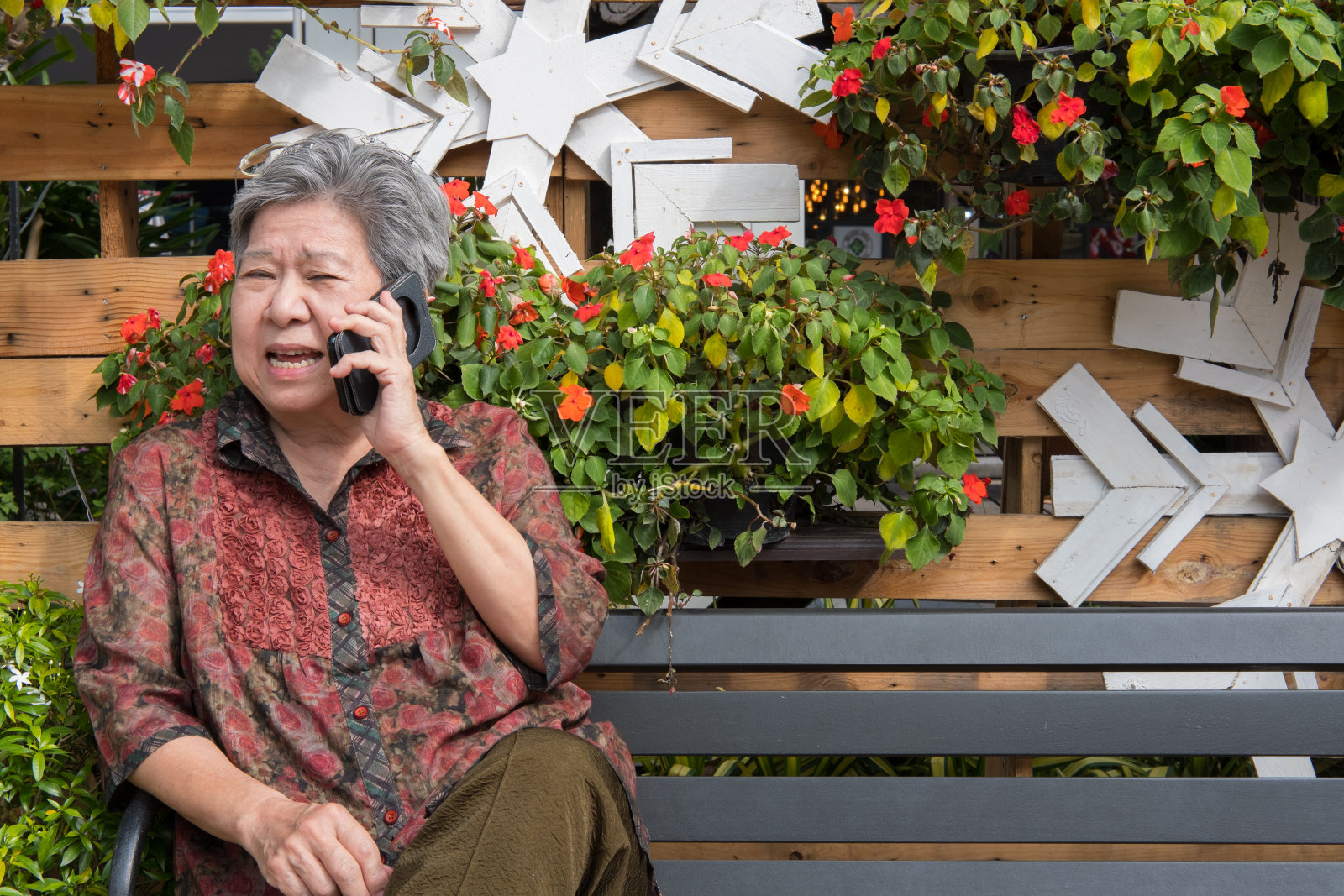 老妇人在花园里讲手机。一位老年女性在公园里用智能手机说话。老年人打电话聊天照片摄影图片