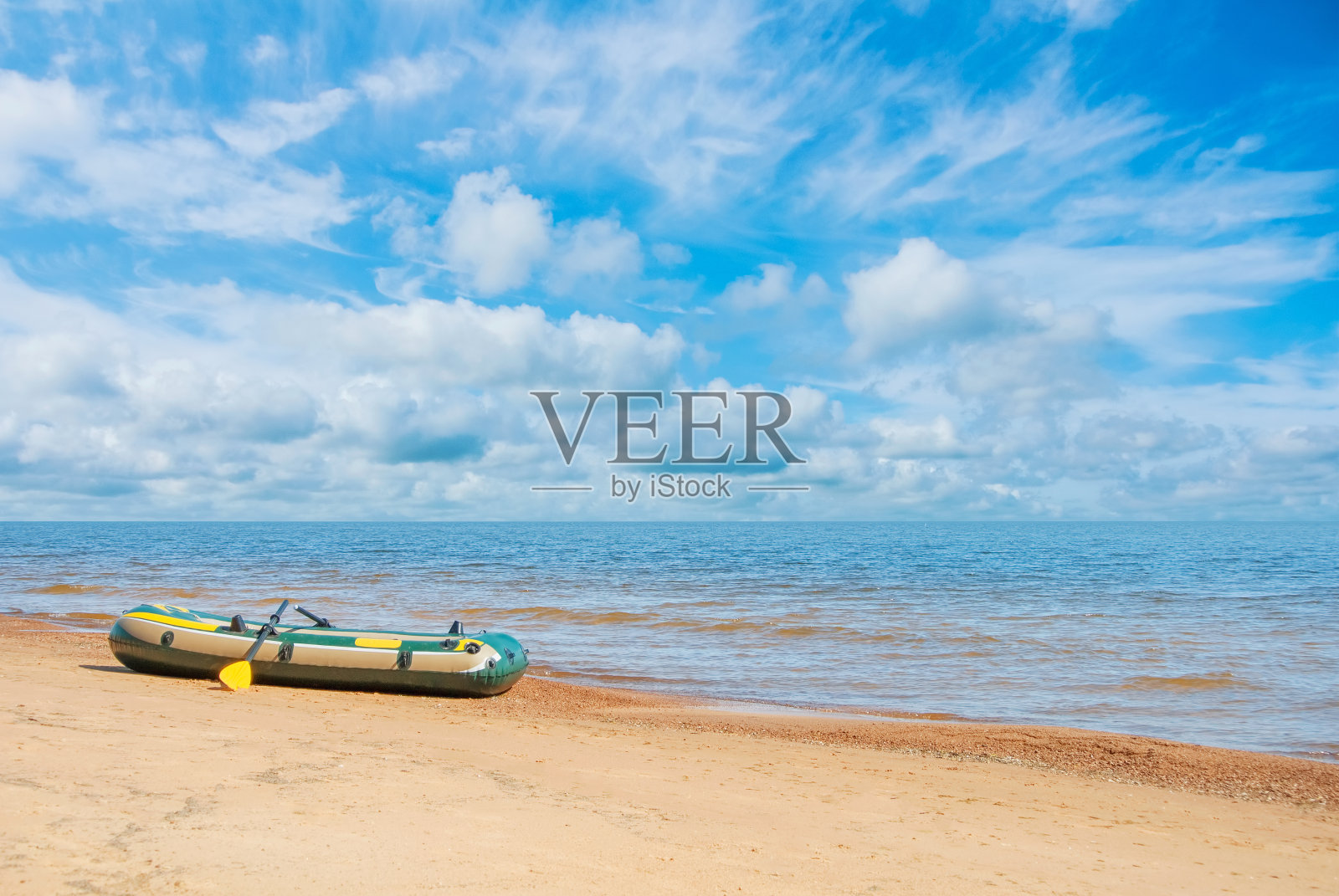 绿色和黄色的充气船与桨站在沙滩海岸,海浪的海景和美丽的戏剧性的蓝色多云的天空在晴朗的日子。度假海边概念,复制文字空间。照片摄影图片
