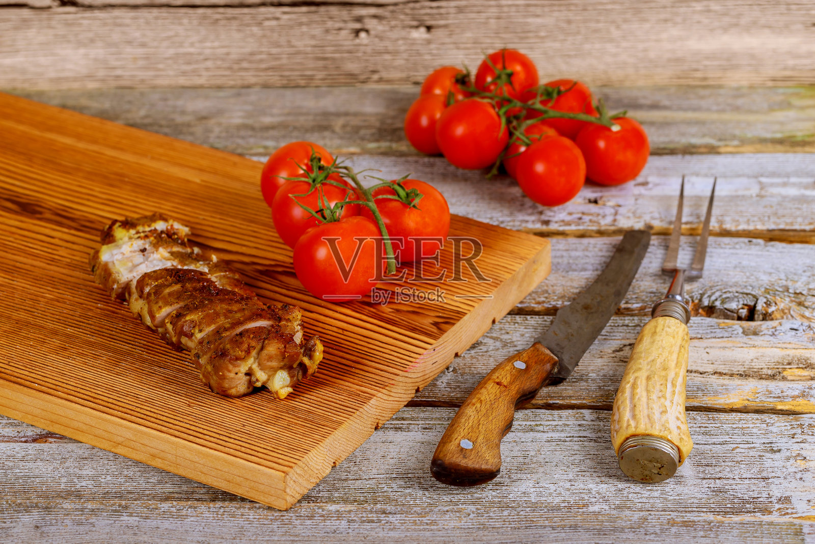 近距离拍摄木桌上的烤猪肉排,旁边是樱桃番茄照片摄影图片