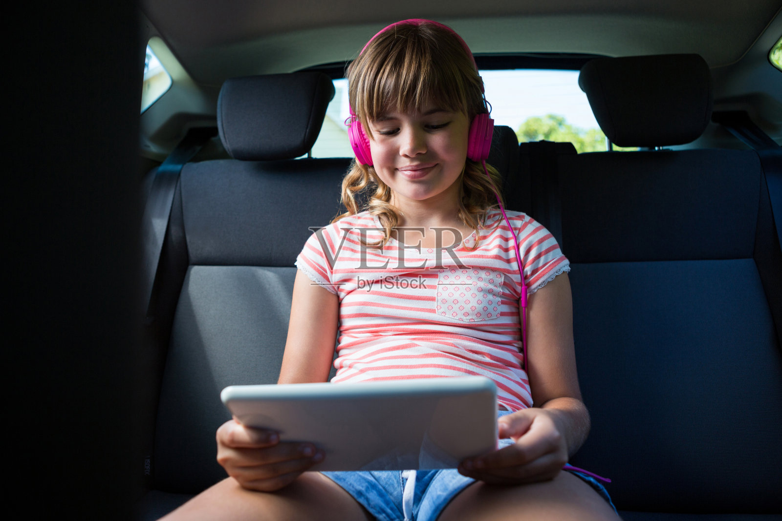 十几岁的女孩戴着耳机在汽车后座上使用平板电脑照片摄影图片
