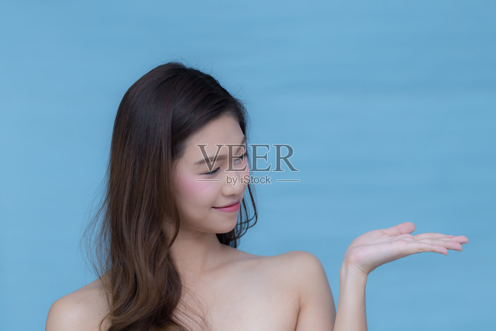 亚洲美女指着蓝色背景上有拷贝空间的东西照片摄影图片