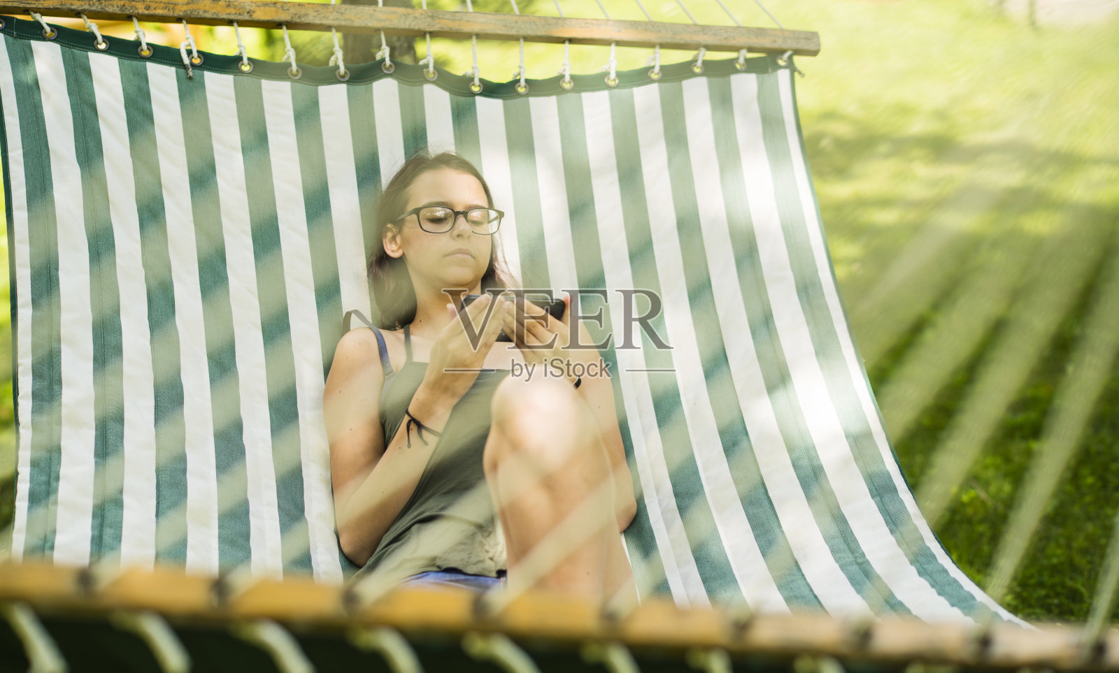 躺在后院吊床上的少女在浏览社交媒体照片摄影图片