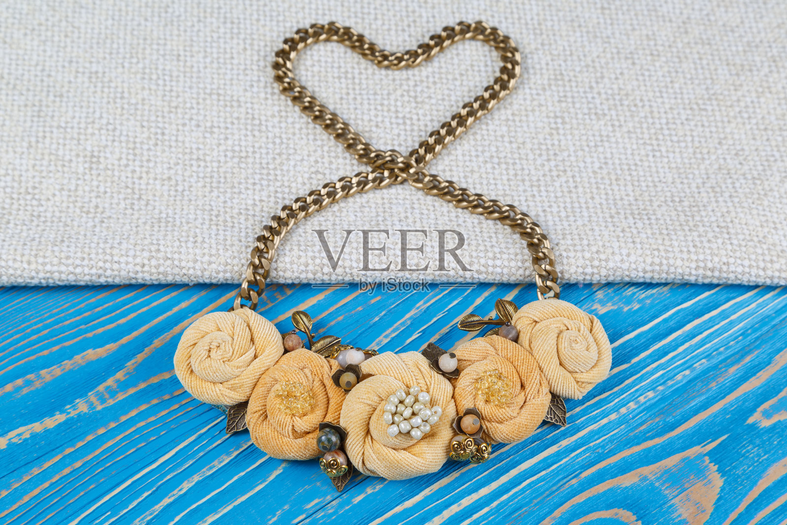 一条金链上的手工项链,摆成一颗心的形状,躺在蓝色的木制背景上照片摄影图片