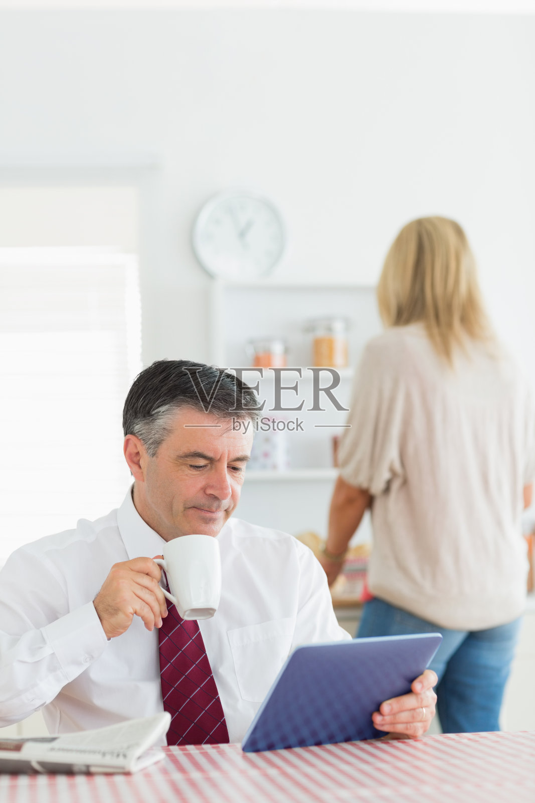 一个男人坐在厨房里,拿着平板电脑,喝着咖啡照片摄影图片