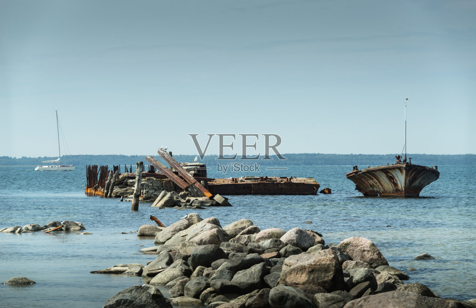 岸边破旧的船只残骸,蓝色的大海和帆船为背景。Harilaid,欧洲爱沙尼亚的一个小岛。照片摄影图片