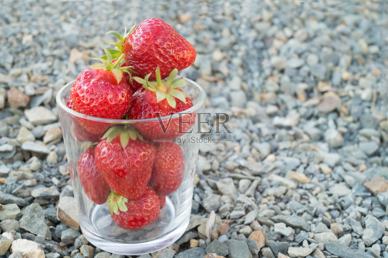 盛满红草莓的玻璃杯立在压碎的灰色石头上。照片摄影图片