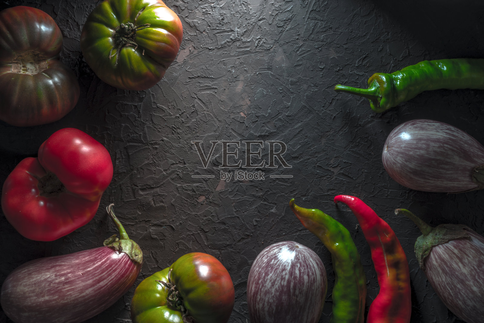 灰色的桌子上放着五颜六色的西红柿、茄子和辣椒照片摄影图片