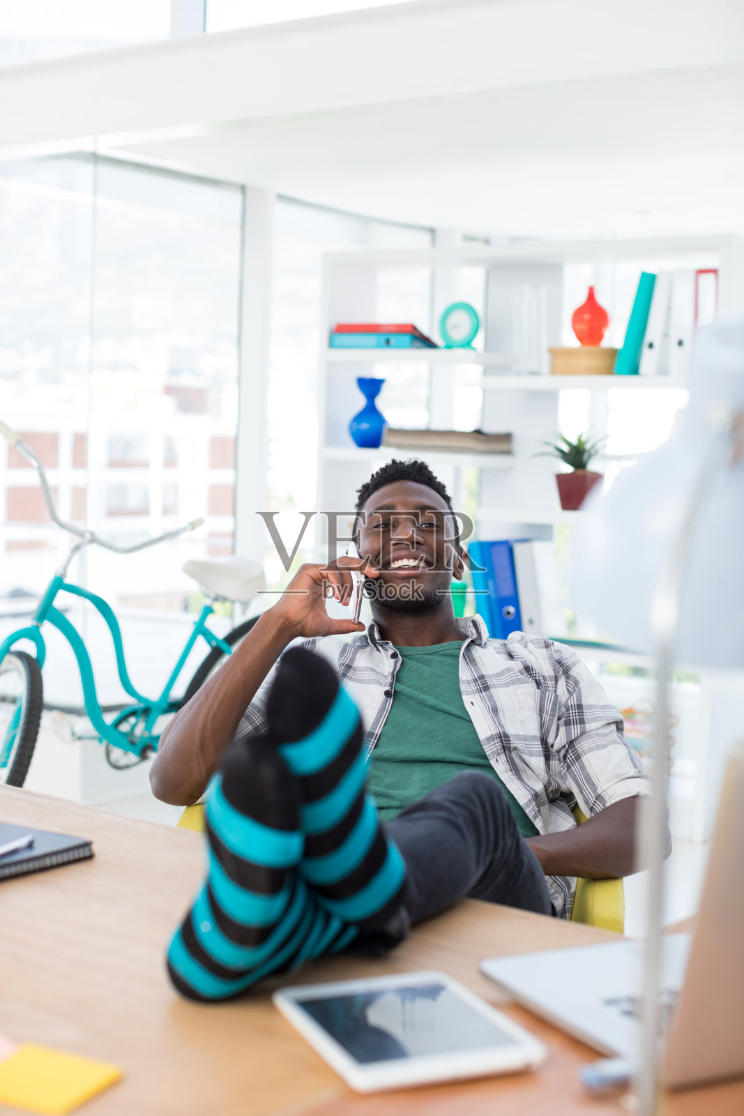 一名男性主管一边在办公室的办公桌前放松,一边用手机打电话照片摄影图片