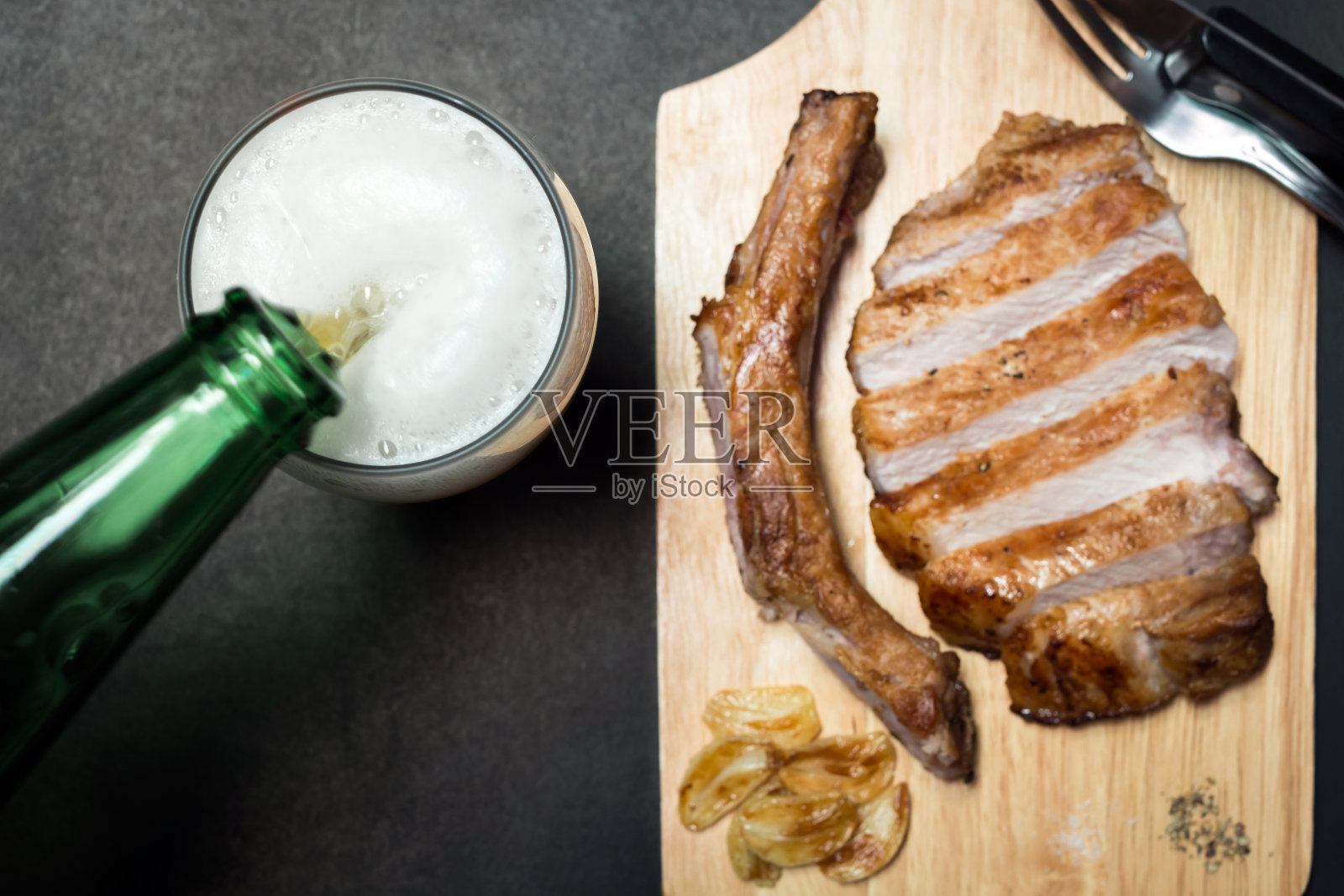 将啤酒倒入高脚杯,配上美味的猪排、香料和烤大蒜。照片摄影图片