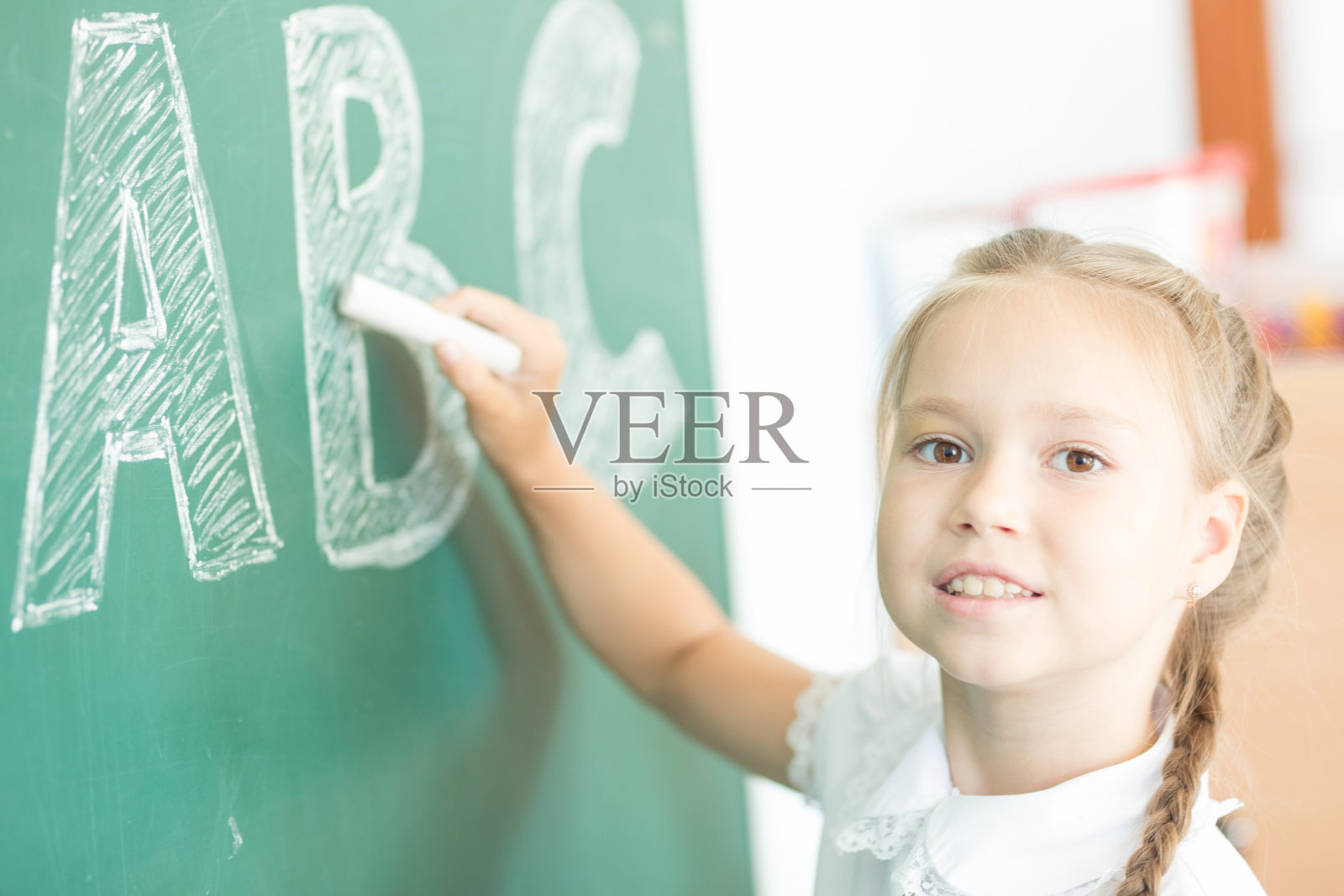 年轻的女孩在绿色的黑板上写ABC照片摄影图片
