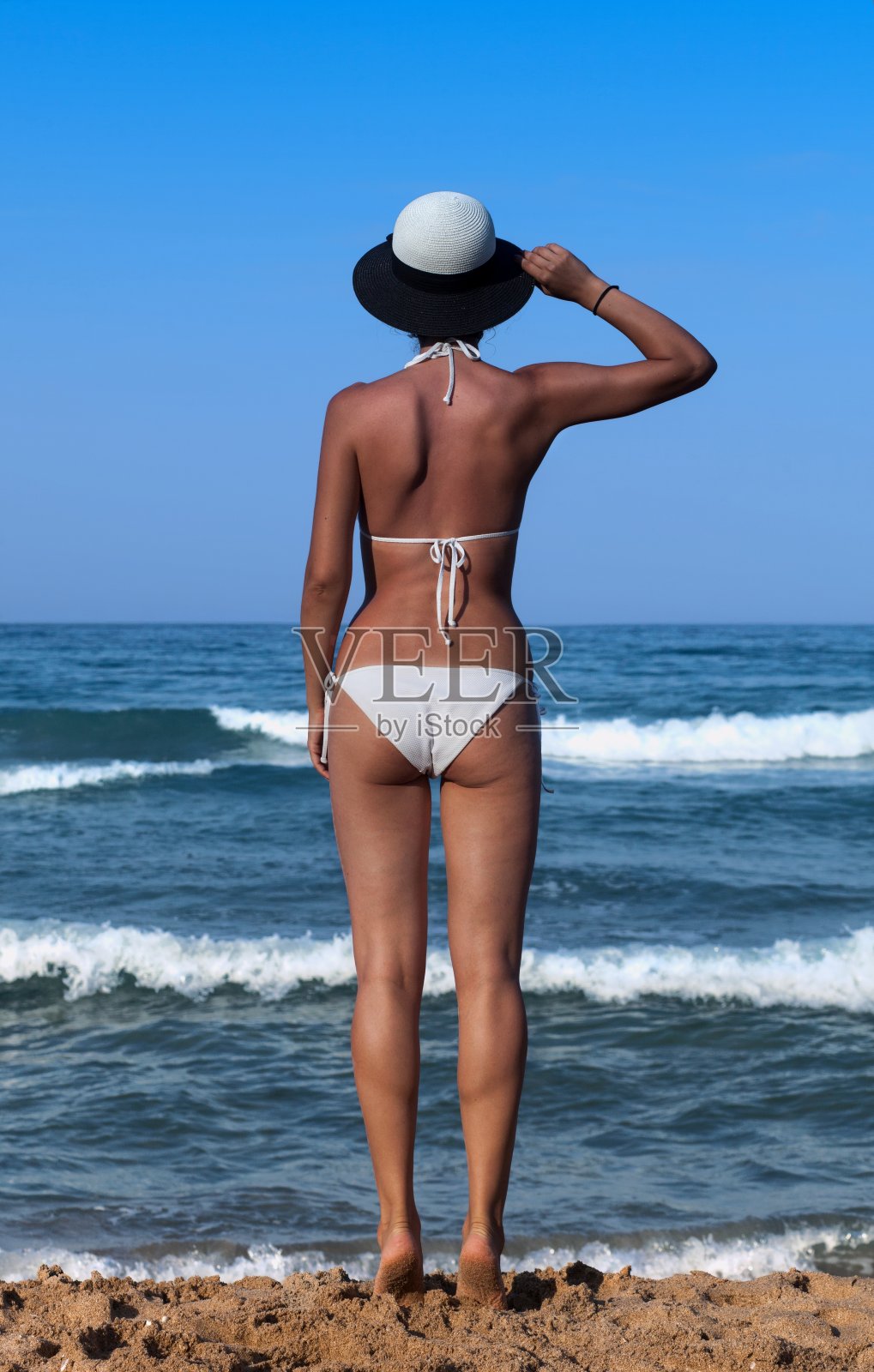 年轻女子穿着白色泳衣在海边晒太阳。照片摄影图片