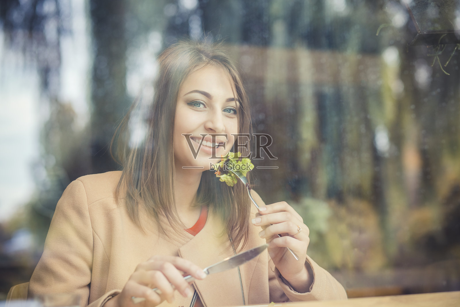 女人幸福的吃。特写肖像美丽的微笑露齿的女孩学生看着你的相机吃绿色沙拉咖啡店的背景。健康快乐生活理念照片摄影图片
