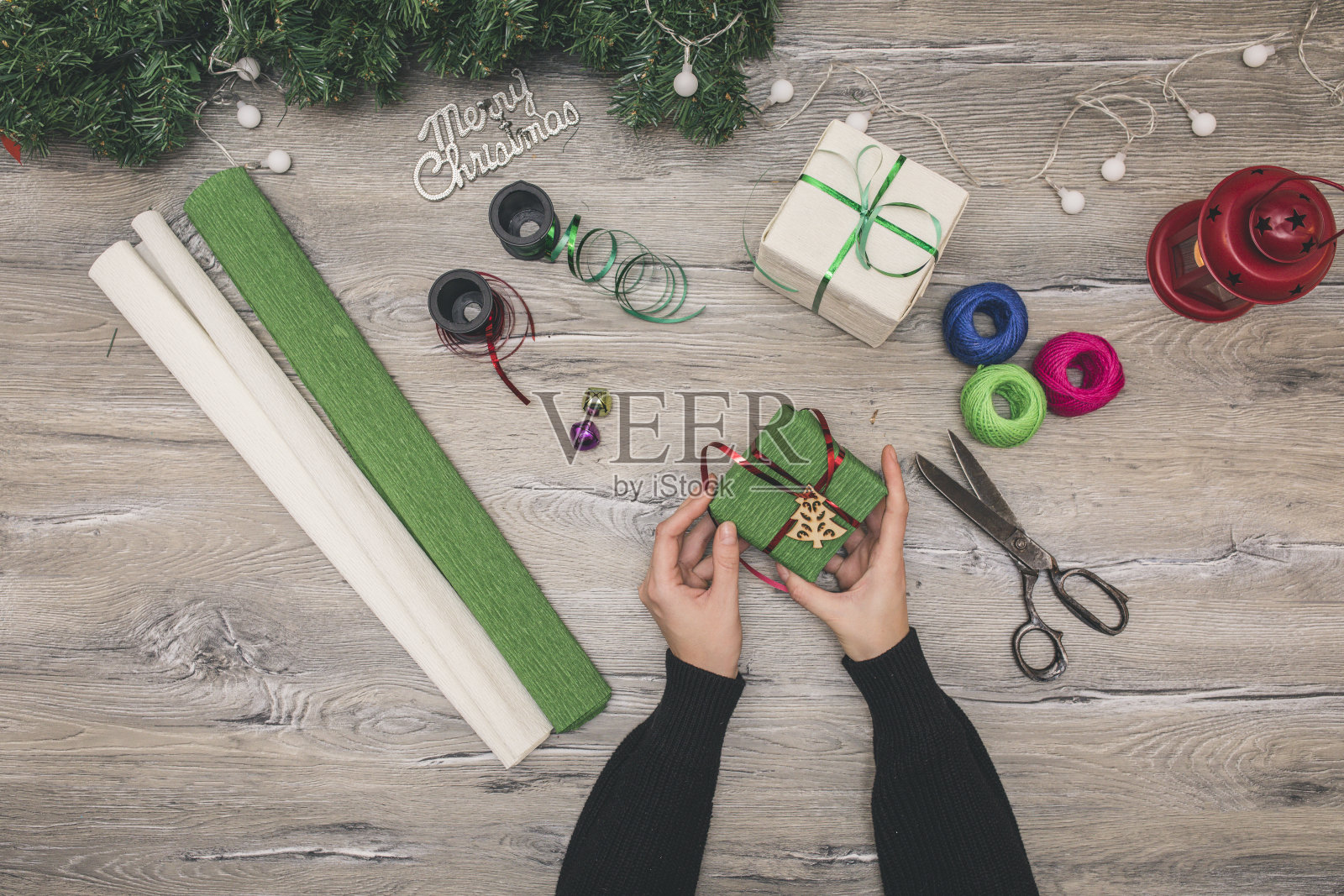 包装圣诞礼物盒。俯视图手放在白色木桌上,用杉木树枝装饰照片摄影图片