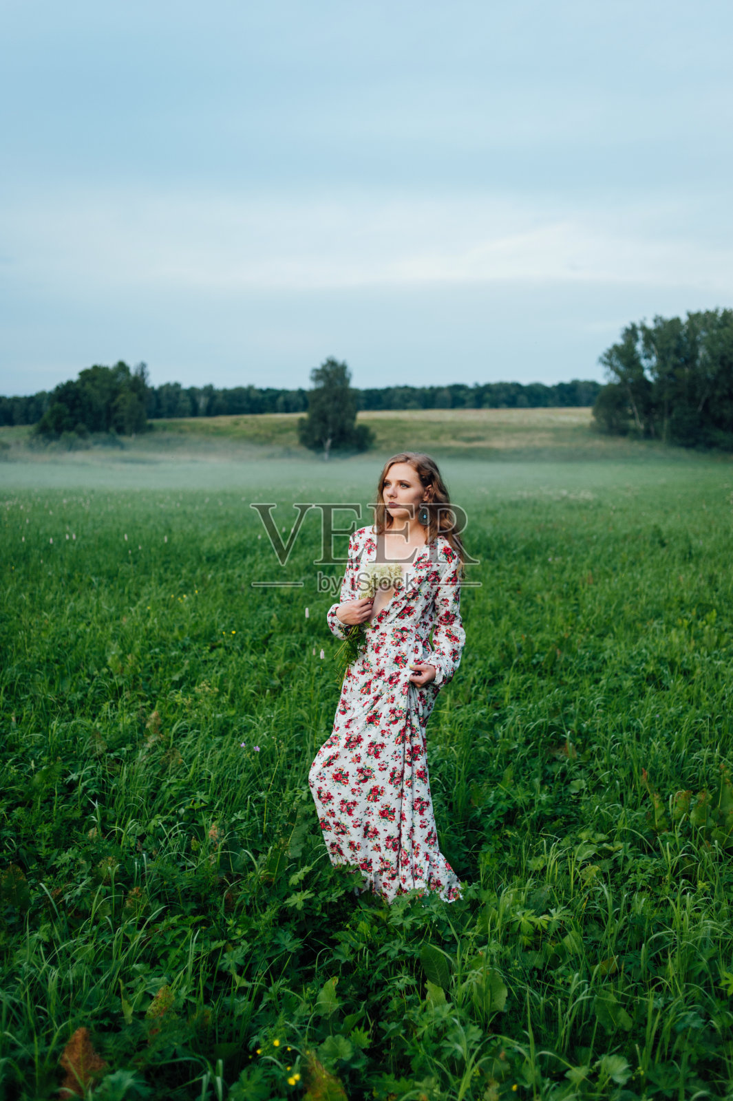 一个美丽的女孩穿着色彩鲜艳的衣服,站在傍晚的草地上,以雾为背景。照片摄影图片