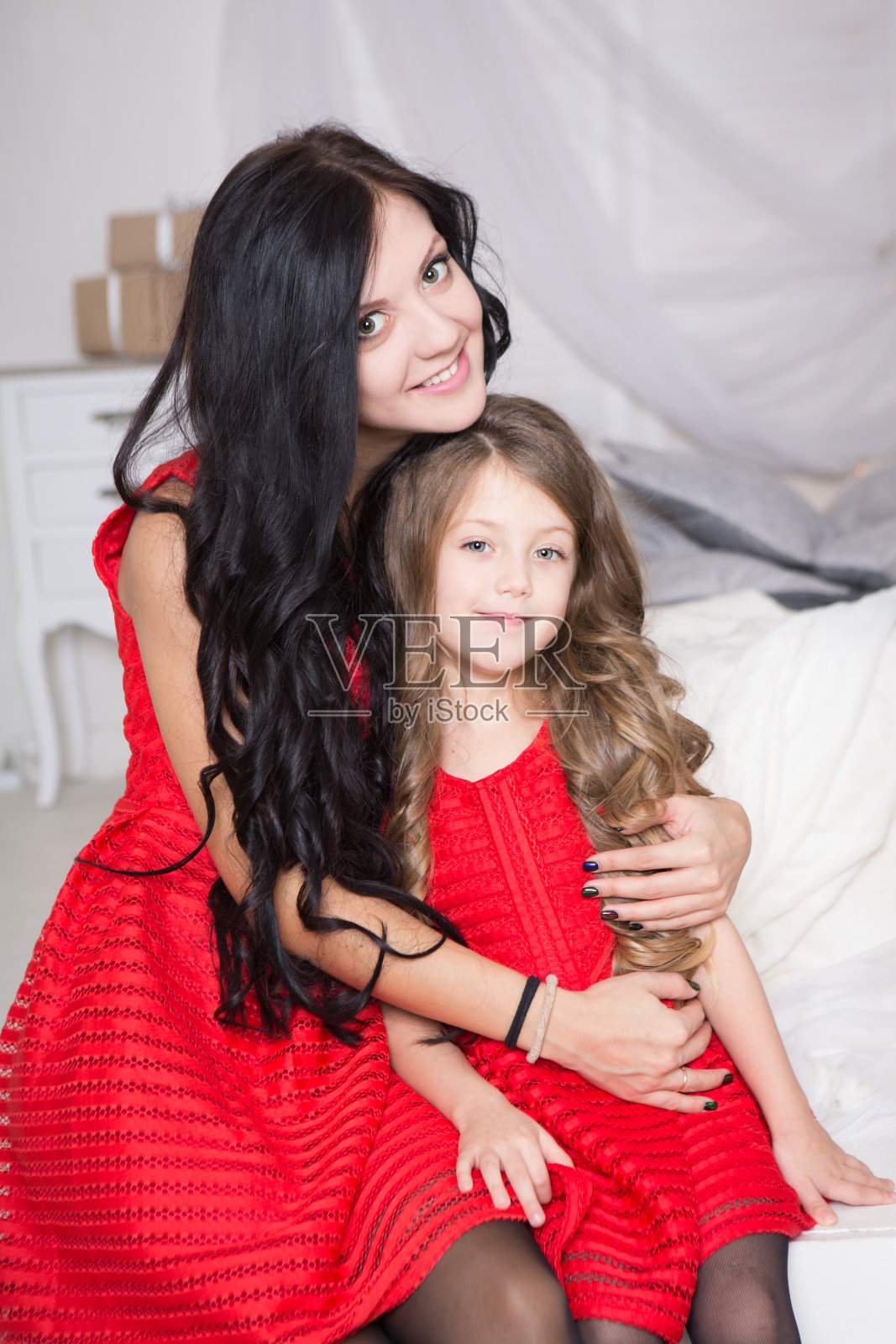 幸福的家庭妈妈和女儿穿着红色的裙子在家里拥抱。家人看照片摄影图片