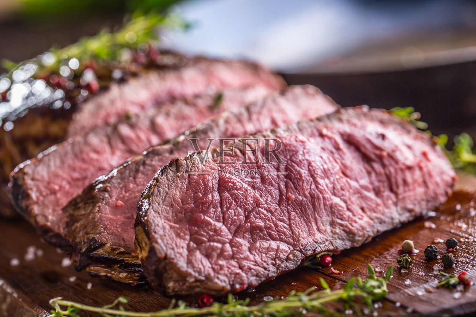 多汁的肋眼牛排木板切片(配叉子、刀、香草和调味料)照片摄影图片