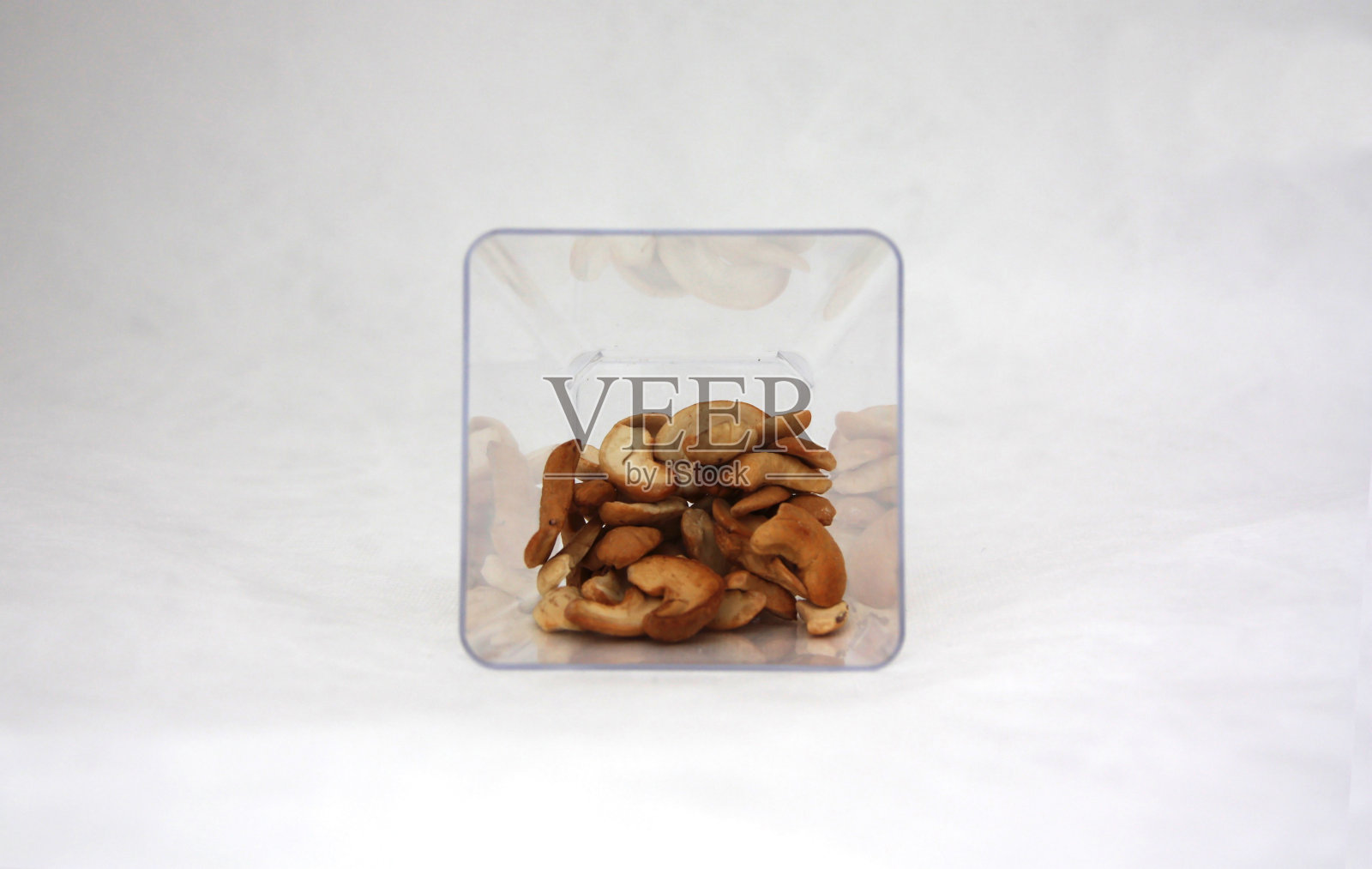 腰果在白色背景的方形塑料罐中。照片摄影图片