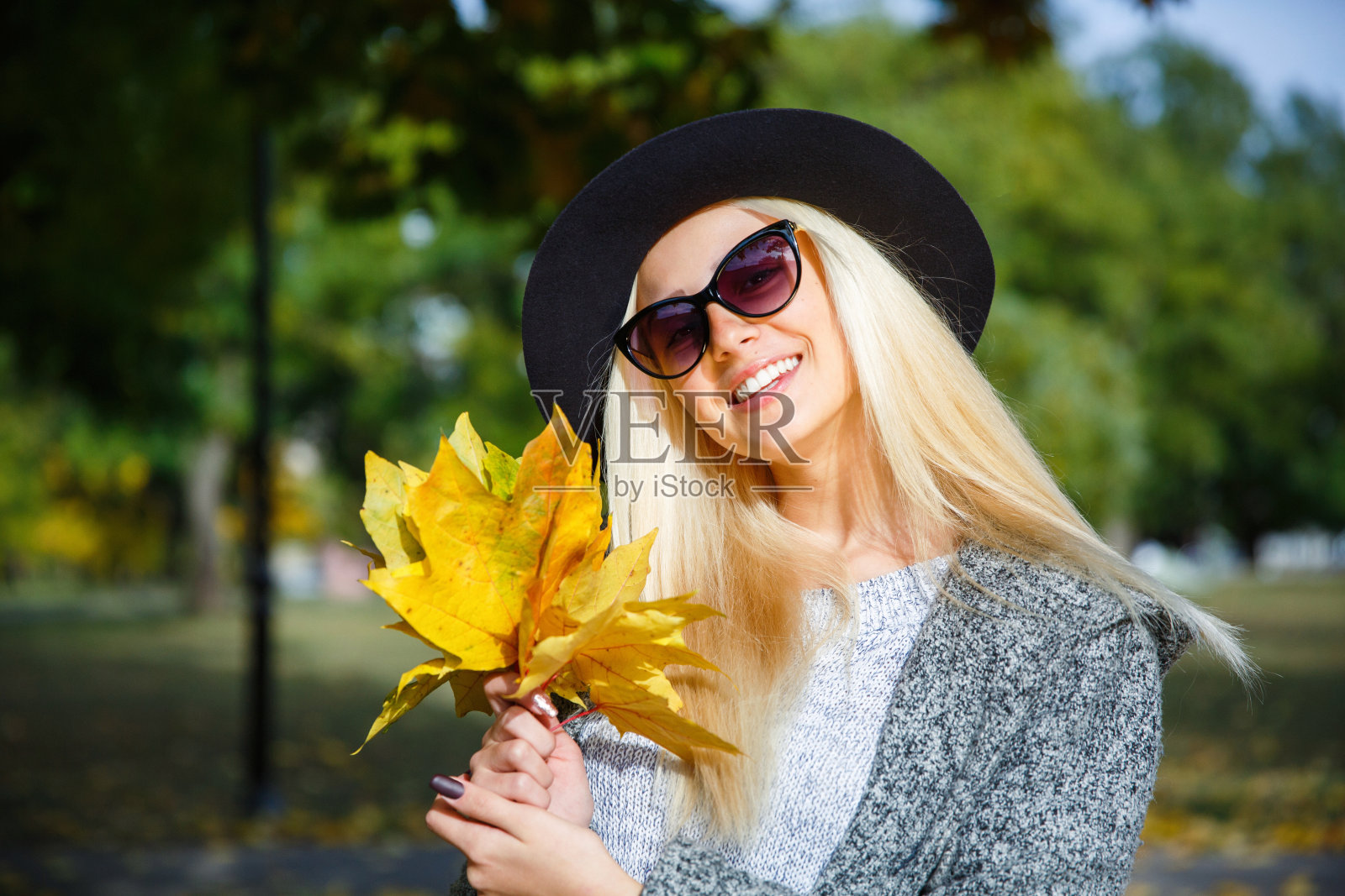 戴眼镜的女孩歪着头,微笑着拿着树上的叶子。照片摄影图片
