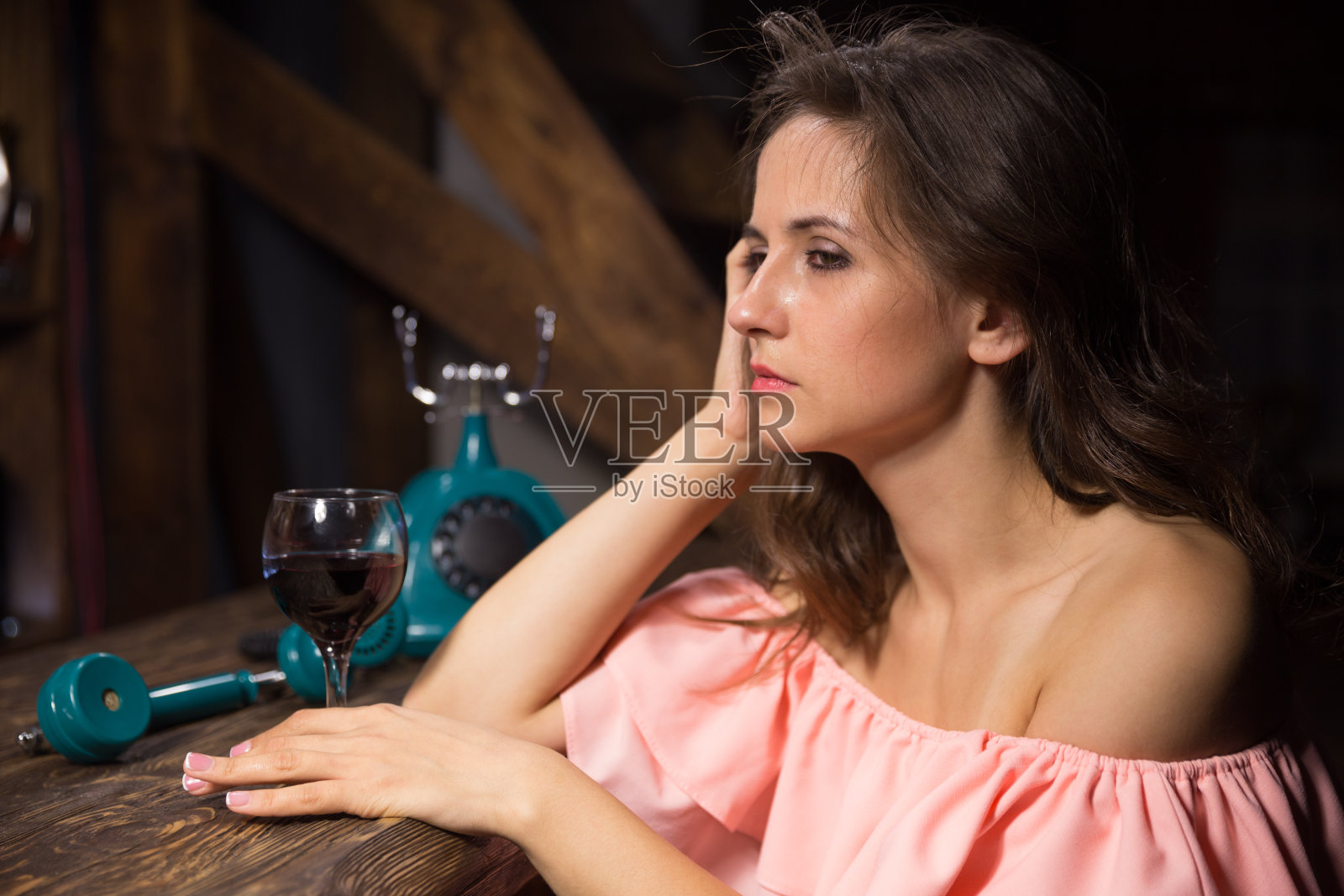 一个悲伤的喝醉了的年轻女人,拿着酒和电话在黑暗的酒吧里照片摄影图片