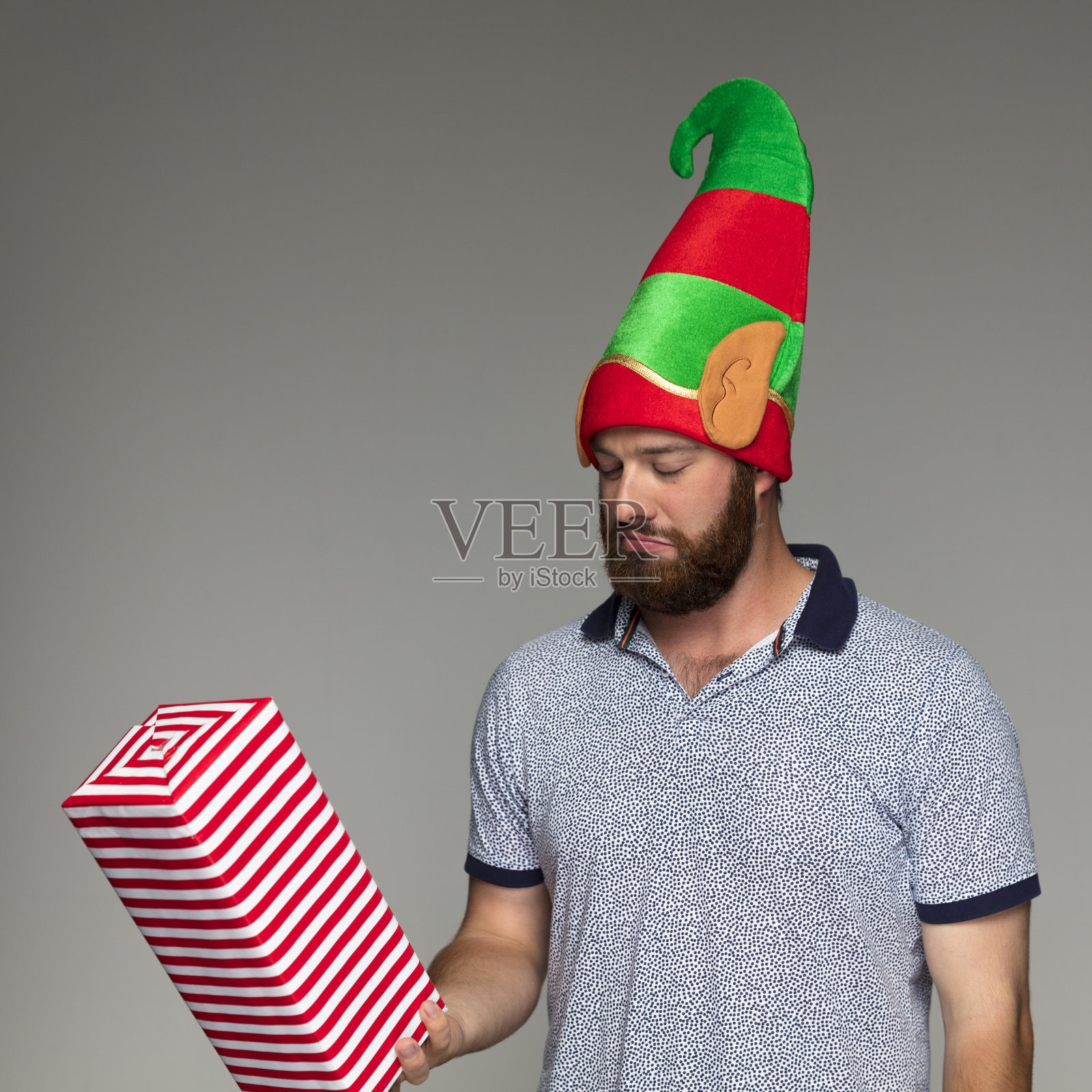 带着圣诞精灵帽子和礼物的悲伤大胡子男人照片摄影图片