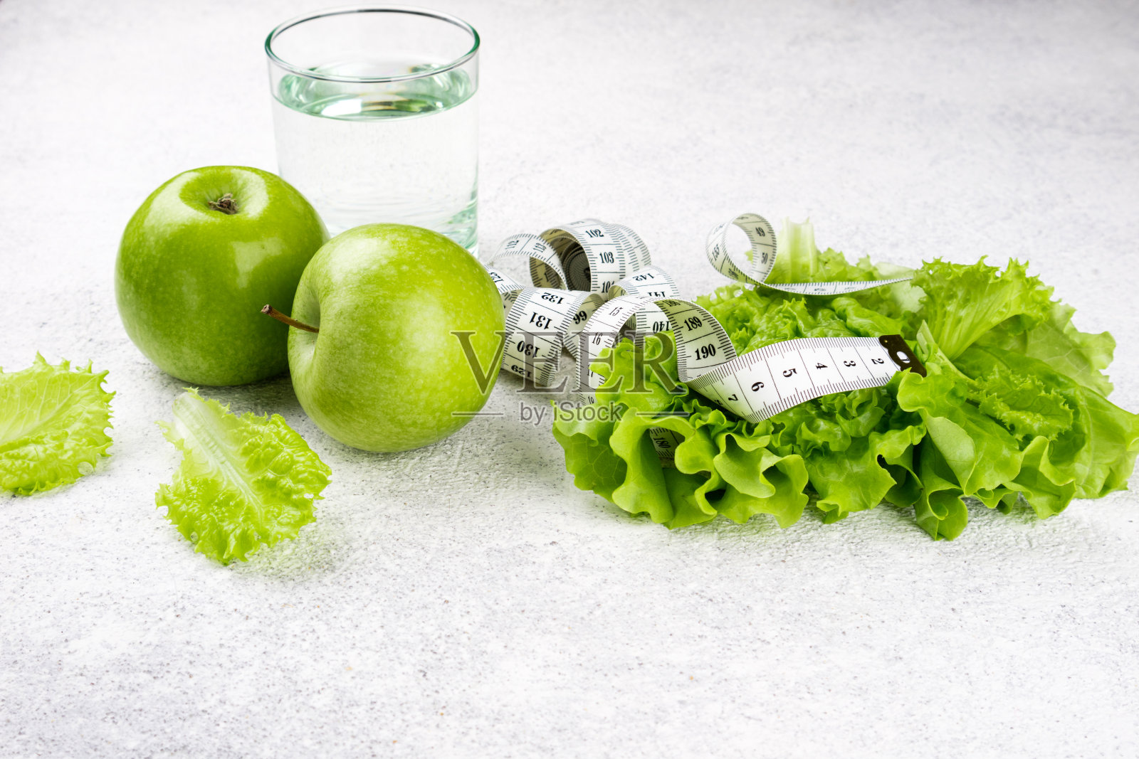 健康饮食。青苹果,生菜沙拉,一杯水,卷尺。节食、瘦身、减肥和饮食计划的概念照片摄影图片