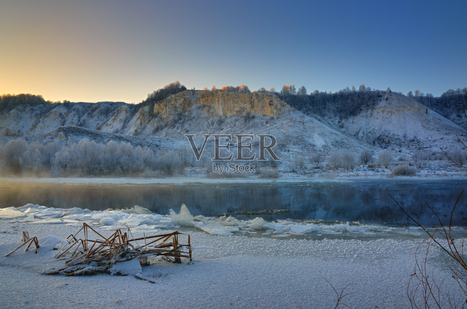 冬天黎明前有霜的早晨。山坡上的河流和大块浮冰结冰了。照片摄影图片