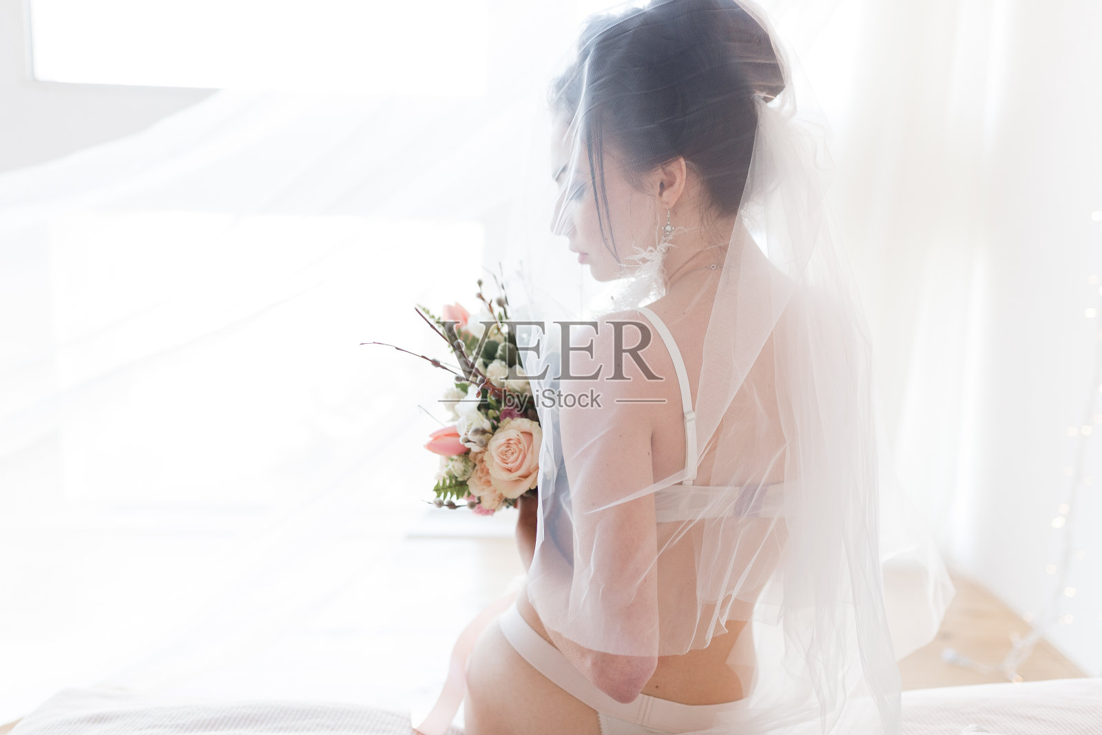 美丽性感时尚的年轻新娘在内衣与漂亮的花束坐在床下面纱。带有拷贝空间的水平视图照片摄影图片