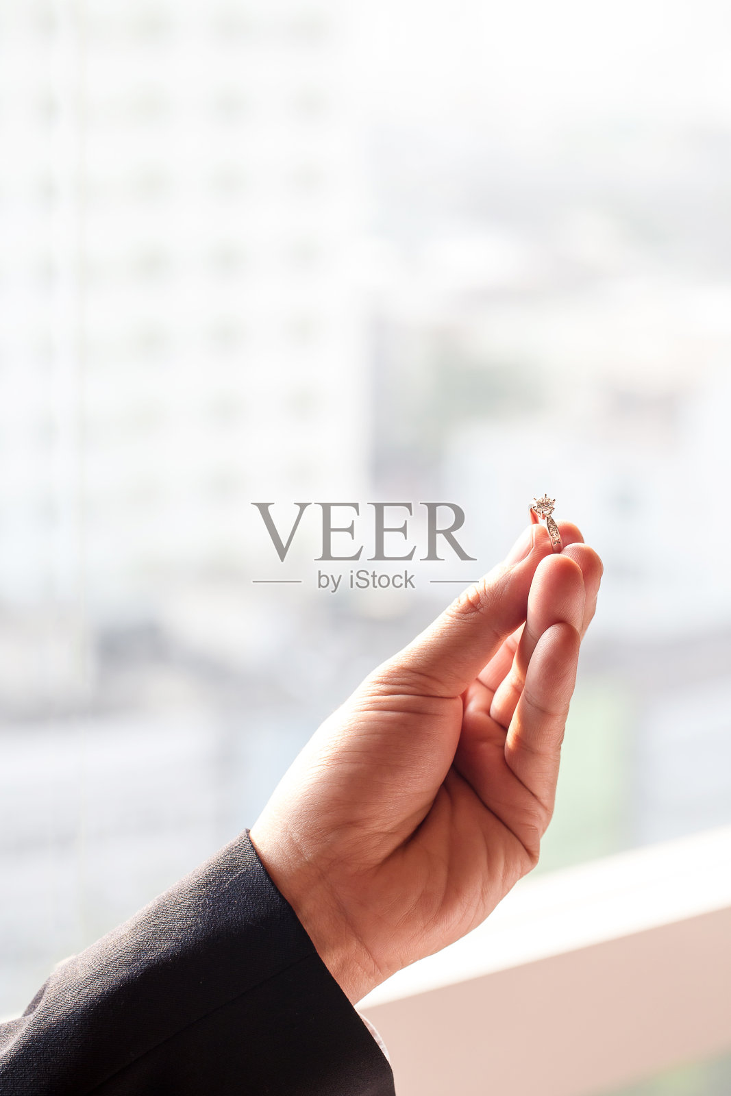 手持钻石戒指与模糊的城市背景。象征着婚礼、婚姻和爱情。照片摄影图片