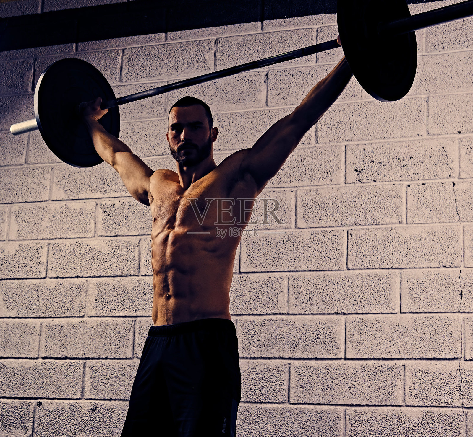 赤裸上身的运动男子在他的头下举着杠铃。照片摄影图片