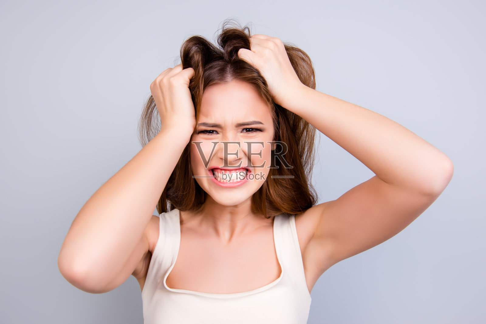 变得越来越疯狂。近距离的肖像大叫紧张的年轻女孩,搞乱她的头发在纯光背景照片摄影图片