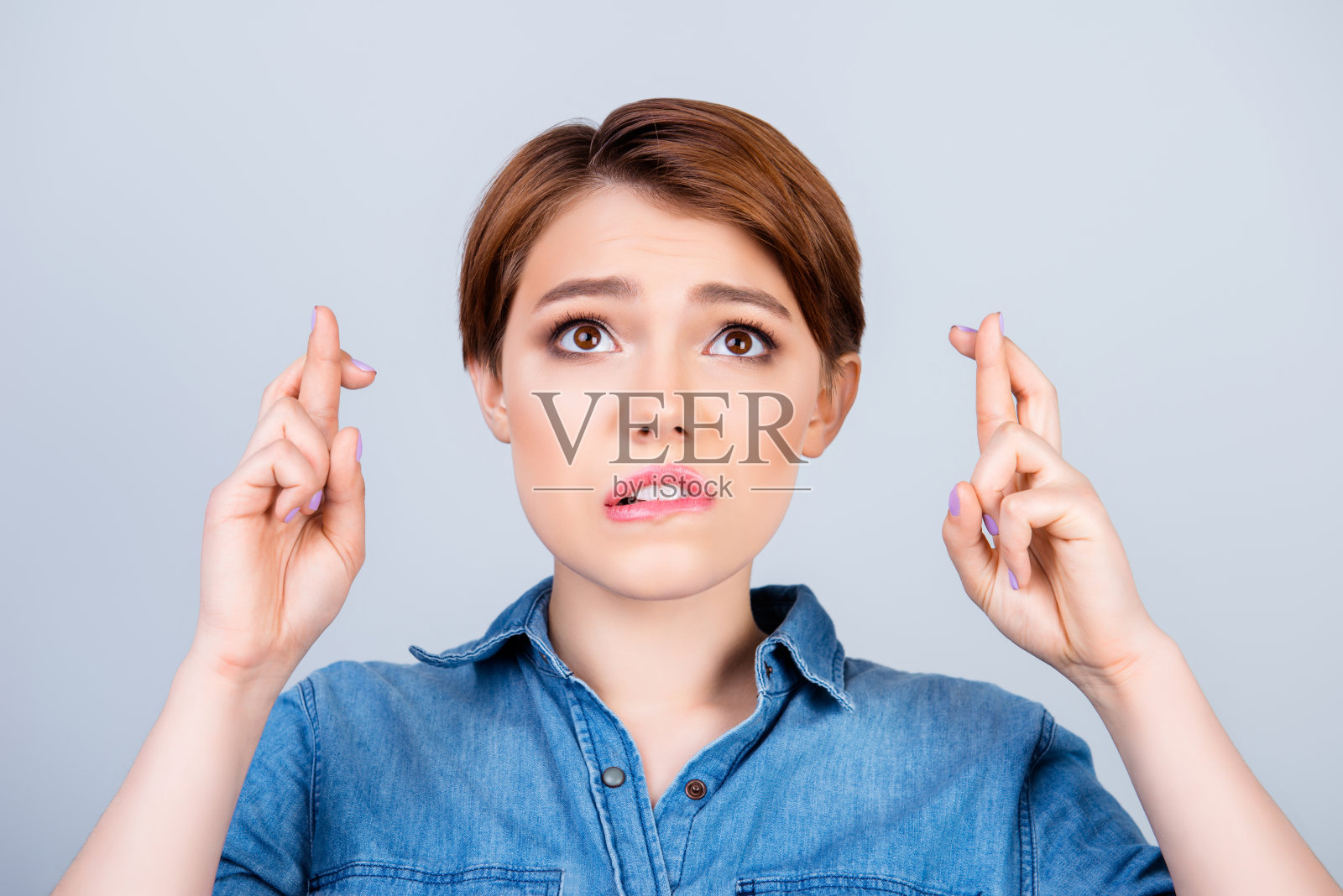 美丽的年轻女子希望她的愿望将实现与交叉手指在浅蓝色的背景上等待照片摄影图片