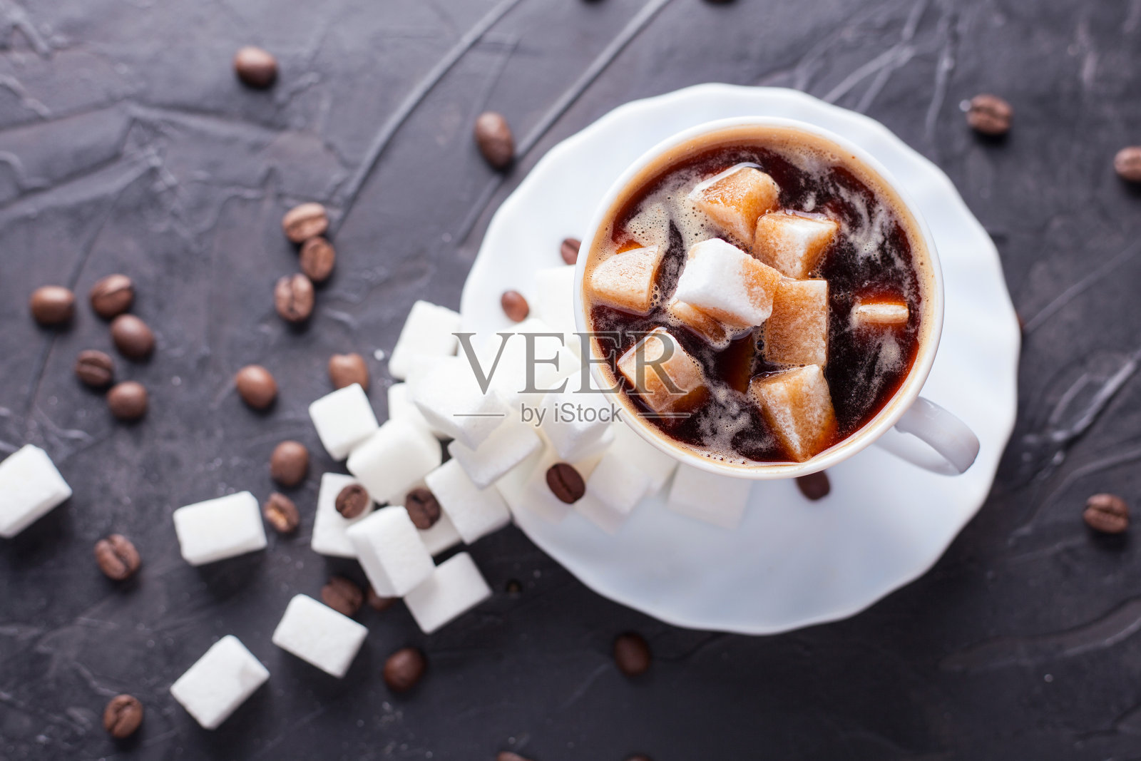 糖成瘾者。在一张黑桌子上的咖啡里放上过多的糖和散落的咖啡豆照片摄影图片