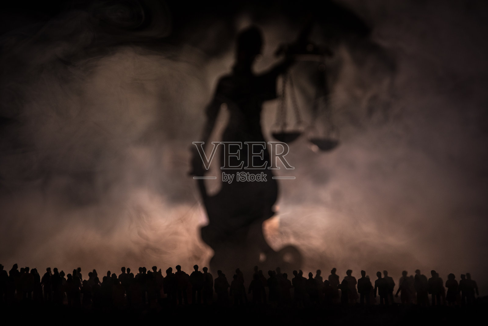 模糊的剪影,巨大的女正义雕像与剑和天平站在人群背后,在夜晚,雾蒙蒙的火的背景。在晚上照片摄影图片