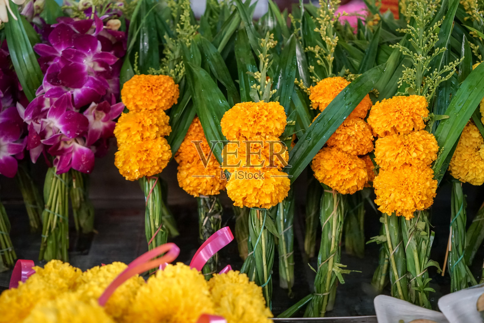 当地市场出售的泰式寺庙供奉鲜花,由黄色万寿菊、紫色兰花和绿叶制成照片摄影图片