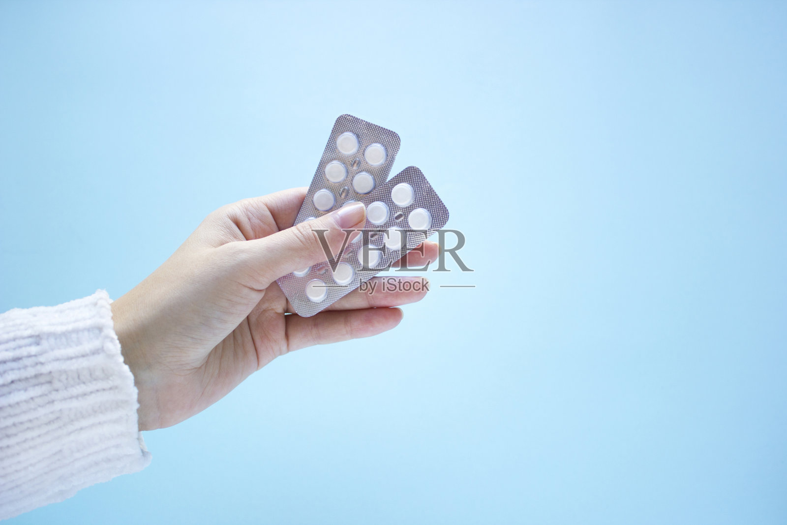 女人手里拿着两包蓝色背景的药片。照片摄影图片