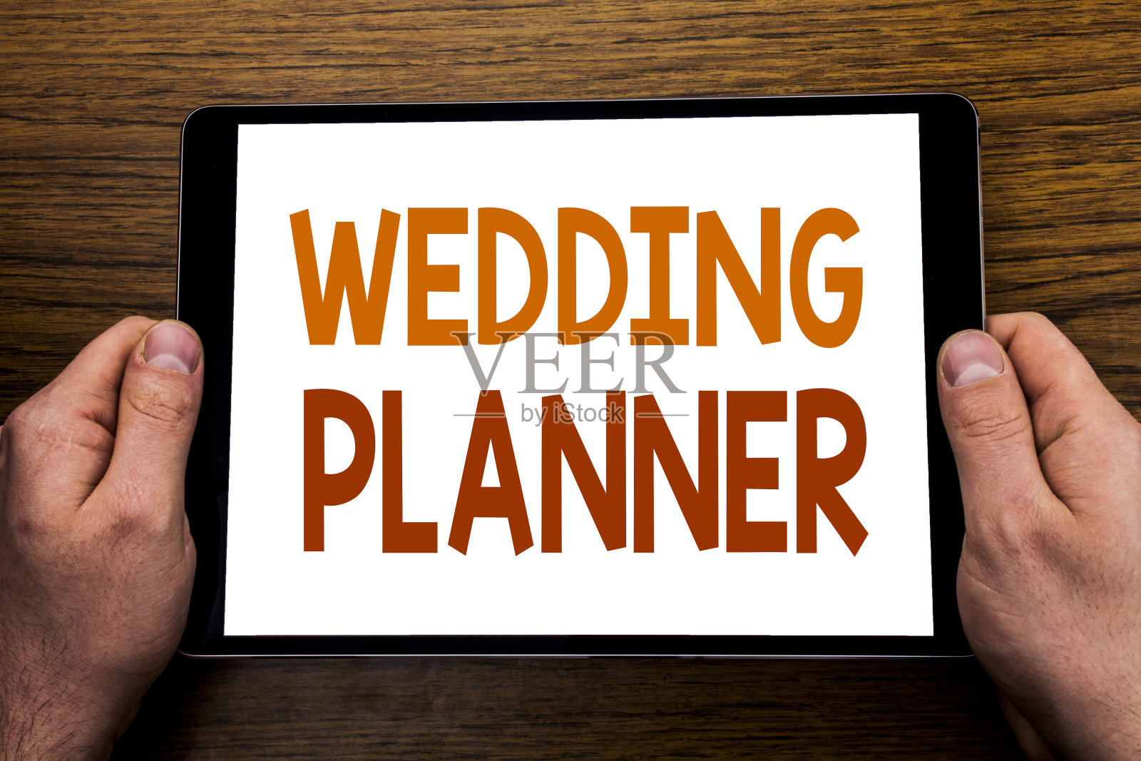 手写文字说明婚礼策划人。写在平板电脑上,木质背景与商人的手,手指握电脑。照片摄影图片