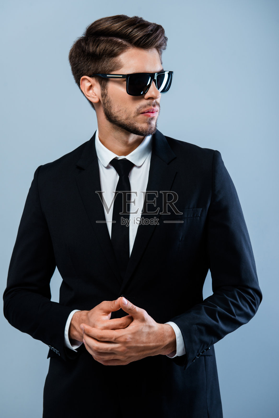 穿着黑西装,戴着眼镜,双手紧握的野蛮男人照片摄影图片