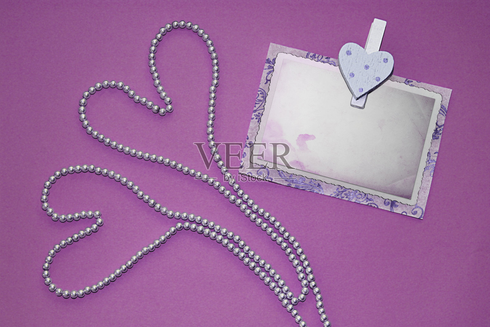 两颗心形珍珠项链和别针与旧相框在不同的颜色背景。照片摄影图片