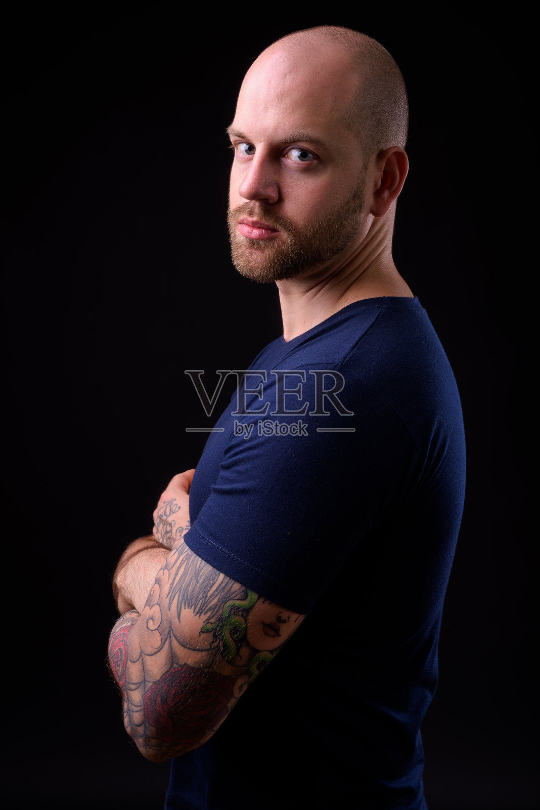 年轻英俊的留着胡子的秃顶男人,纹身映衬着黑色的背景照片摄影图片