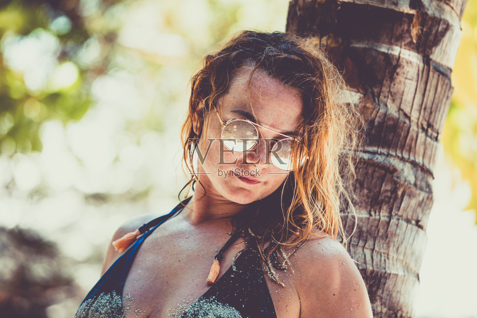 美丽的年轻女子倚在棕榈树上照片摄影图片