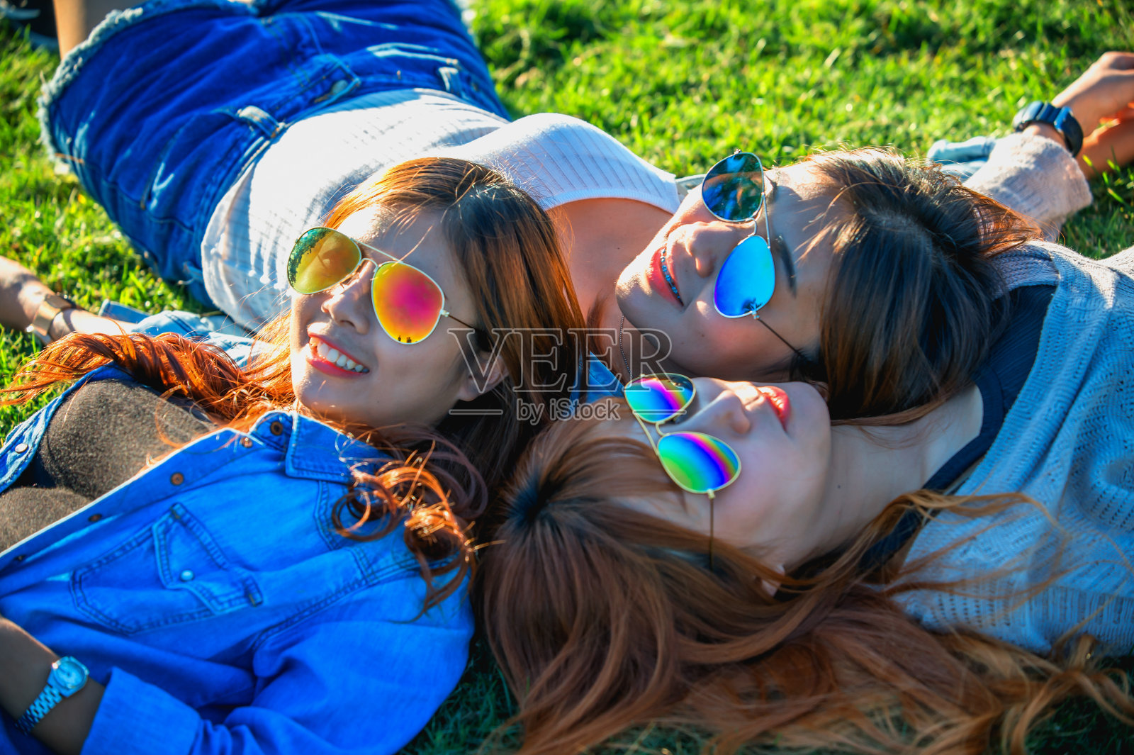 三个亚洲快乐的女孩躺在绿色的草地上戴着太阳镜照片摄影图片