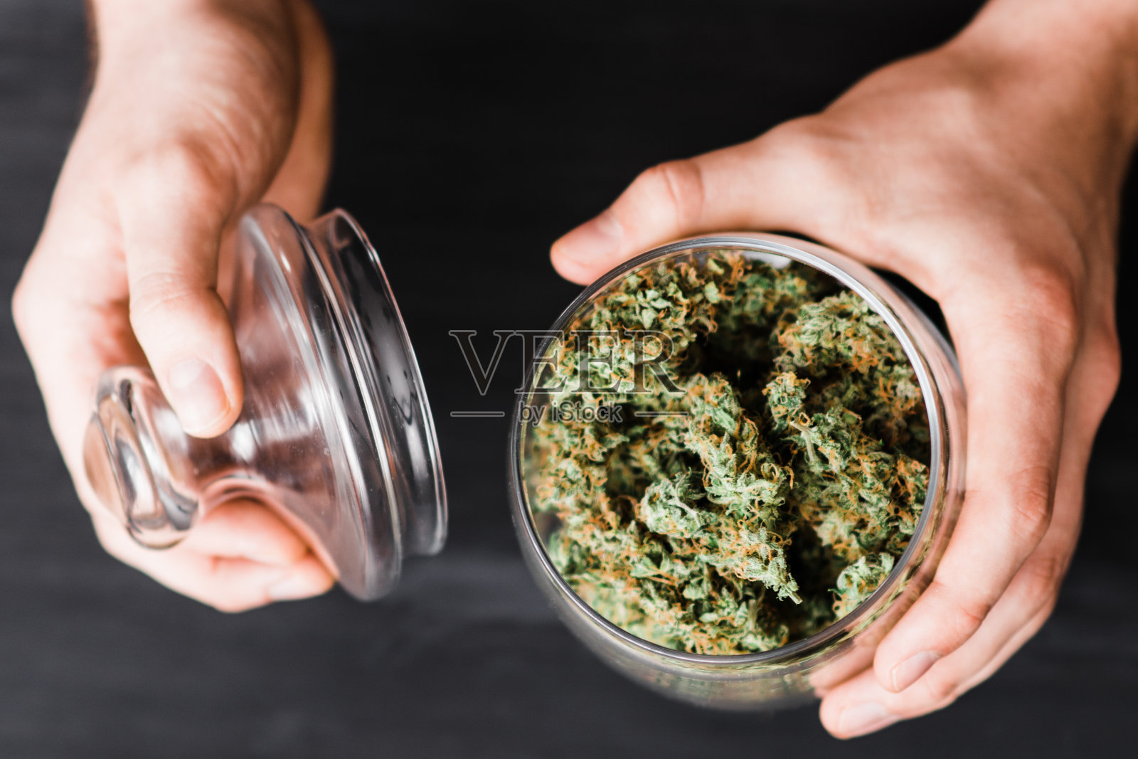 顶视图大麻。一个男人手里拿着大麻花蕾的罐子。照片摄影图片