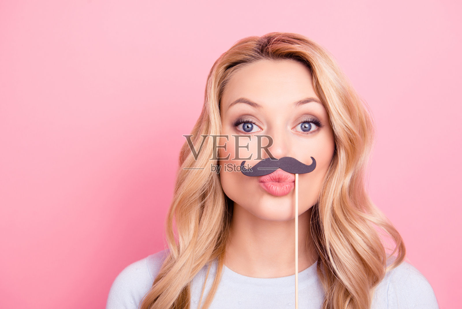 funky调情女孩的肖像与黑色纸盒胡子上的棒子发送飞吻与噘嘴的嘴唇到相机孤立的粉红色背景照片摄影图片