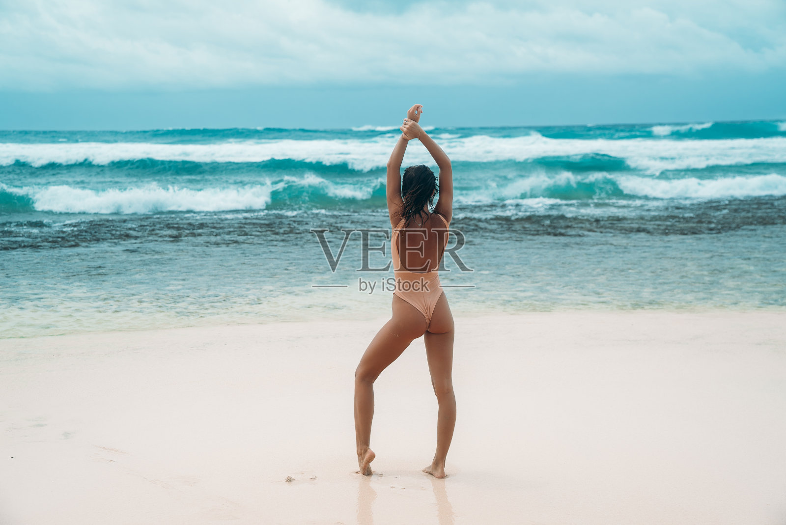 后视图黑发女孩与卷曲的头发在米色泳衣是从事运动的沙滩与白色的沙滩附近的海洋度假。一个美丽的模特与性感的身体是日光浴照片摄影图片